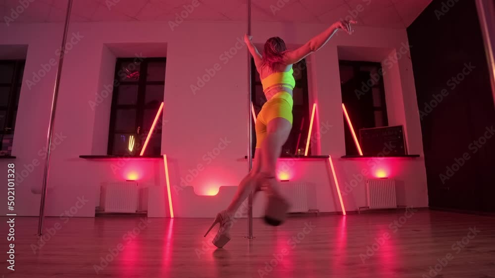 Sexy female pole dancing on red background. Elegant woman dancing near pole with red light at background. Sensual dance. Dance and acrobatics concept. 4K, UHD