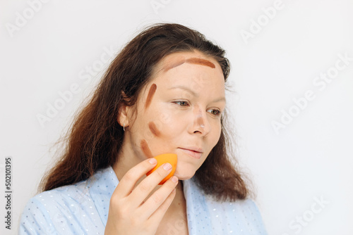 The girl applies bronzer dark corrector on the face with a sponge. photo