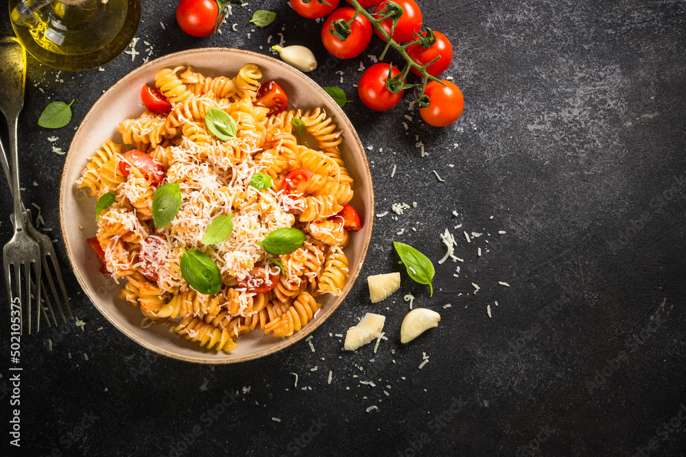 Italian pasta alla arrabiata with fresh tomatoes, basil and parmesan on black stone table. Flat lay with copy space.