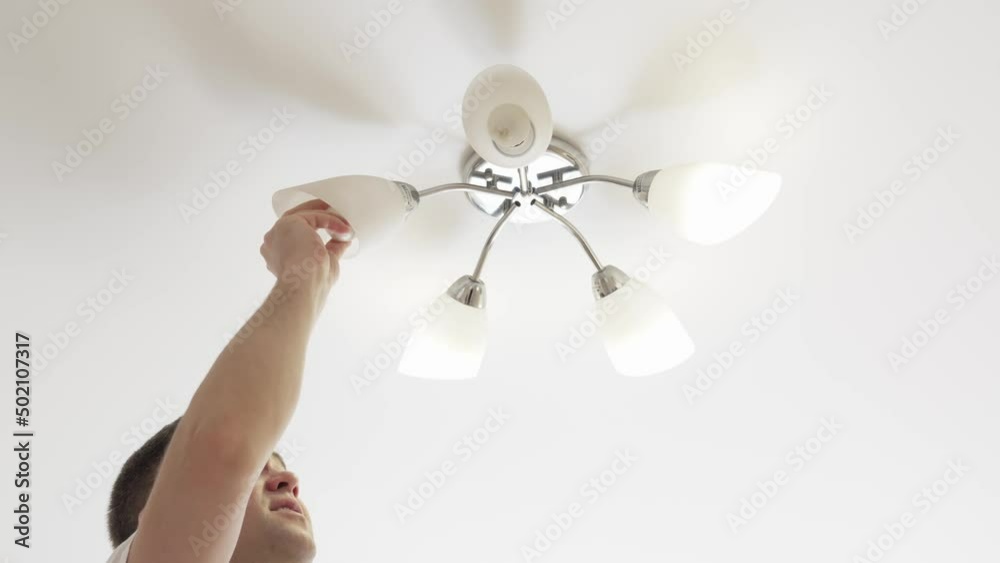 A male electrician changes the light bulbs in the ceiling light. A male electrician changes the light bulbs in the ceiling light.