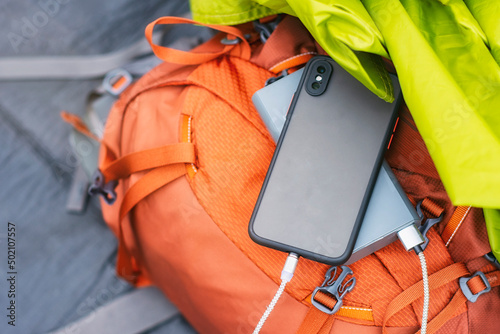 The smartphone is being charged with a portable charger. Power bank with a mobile phone on a sleeping bag with a backpack.