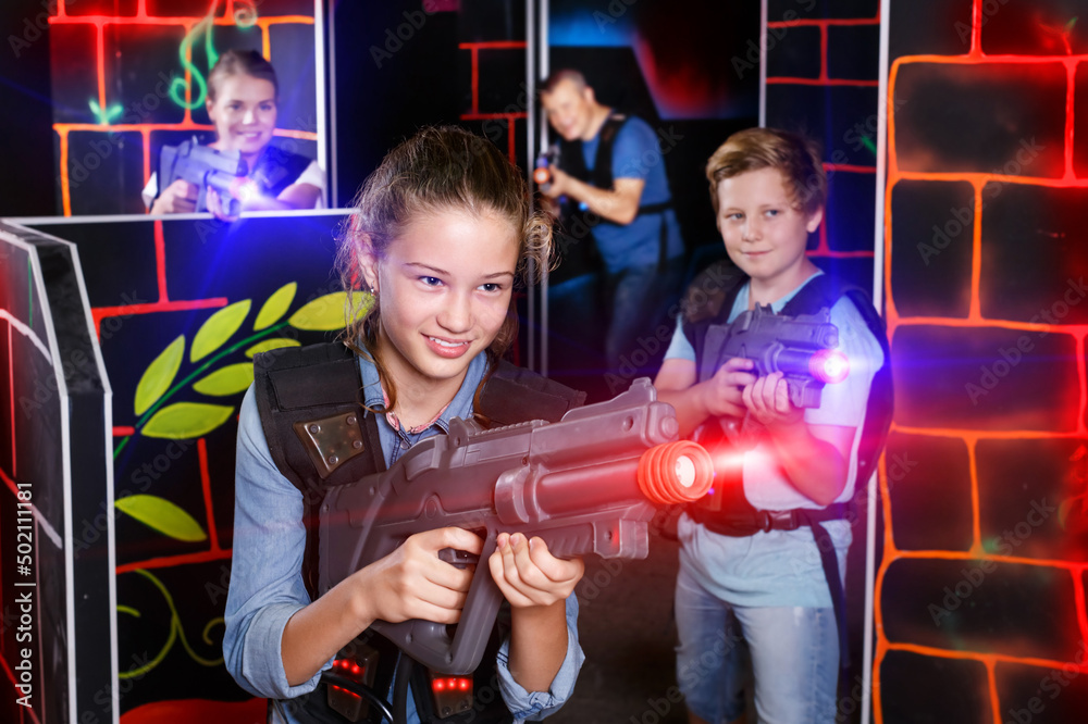 Emotional teen girl with the laser pistol playing laser tag with family at dark labyrinth