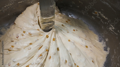 Close up for the prosess of mixing pastry with raisins in metal bowl, nutritious food concept. Stock footage. Raw dough mixing process at the factory.
