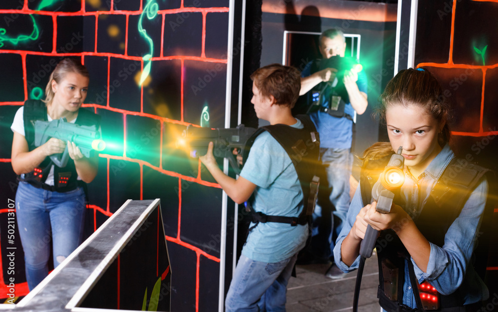 Portrait of cheerful positive smiling teenager girl with laser gun having fun with her family on lasertag arena