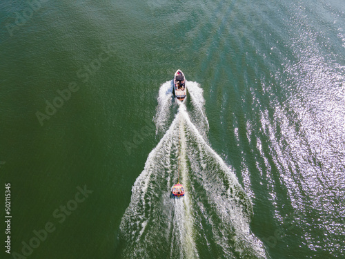 Wakeboard boat that is pulling a tube with people on it. Tubing on a wide open lake in summer time.