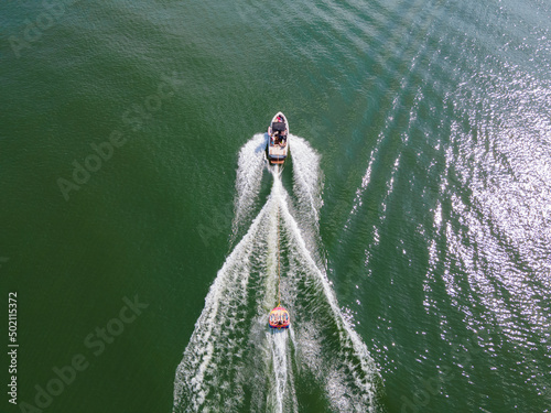 Wakeboard boat that is pulling a tube with people on it. Tubing on a wide open lake in summer time.