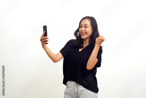 Successful asian young woman standing while holding a cell phone. Isolated on white background
