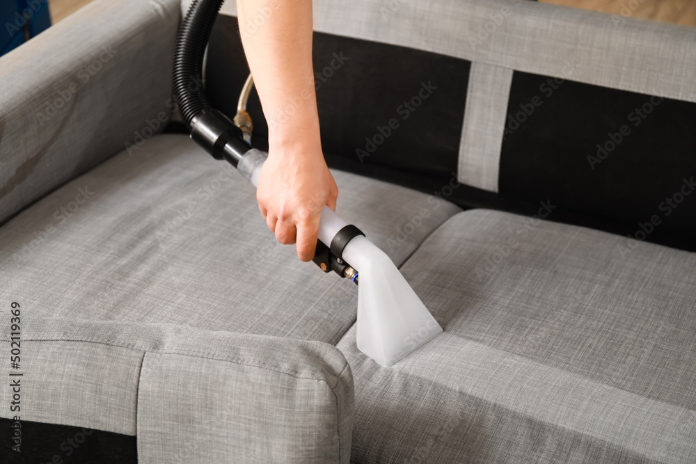 Man removing dirt from grey sofa with vacuum cleaner in room, closeup