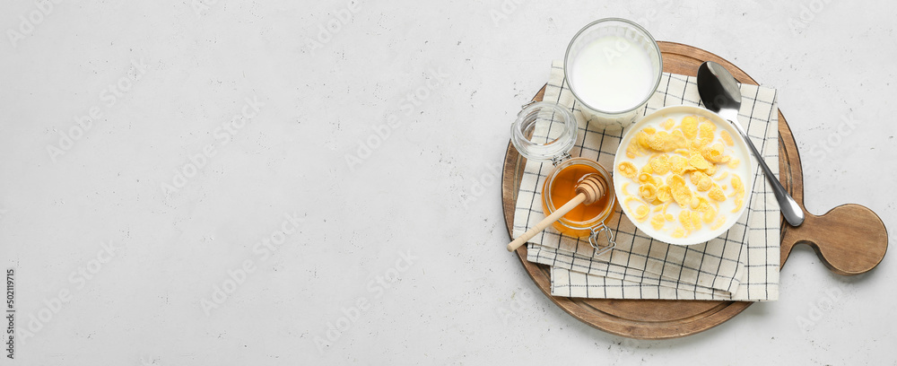 Bowl of crunchy corn flakes with milk and honey on light background with space for text