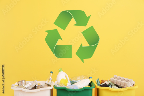Containers with different types of garbage and symbol of recycling on yellow background