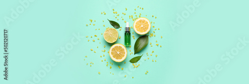 Photo Bottle of natural serum, green leaves, lemon, lime and sea salt on turquoise background