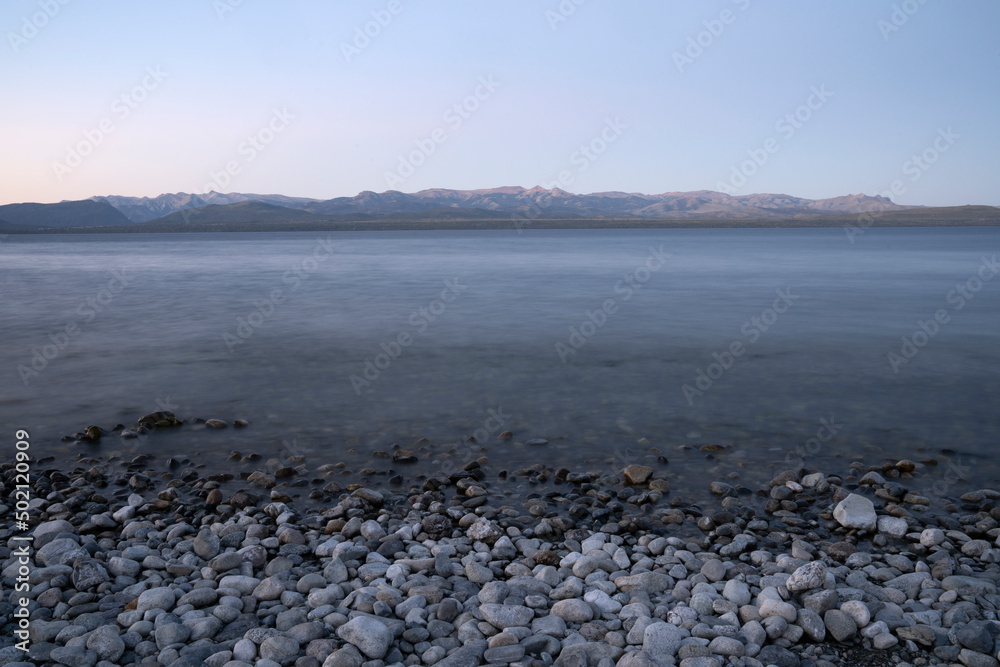 Long exposure shot of Nahuel Huapi lake at sunset. Beautiful blurred water effect, the rocky shore and Andes mountains in the horizon with a magical dusk light. Long exposure shot of Nahuel Huapi lake at sunset. Beautiful blurred water effect, the rocky shore and Andes mountains in the horizon with a magical dusk light.