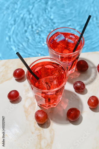 Glasses of fresh grape soda on edge of swimming pool