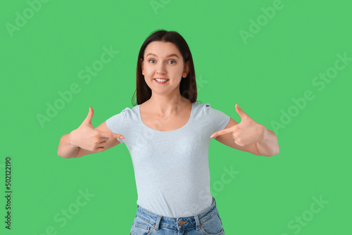 Young woman pointing at t-shirt on green background