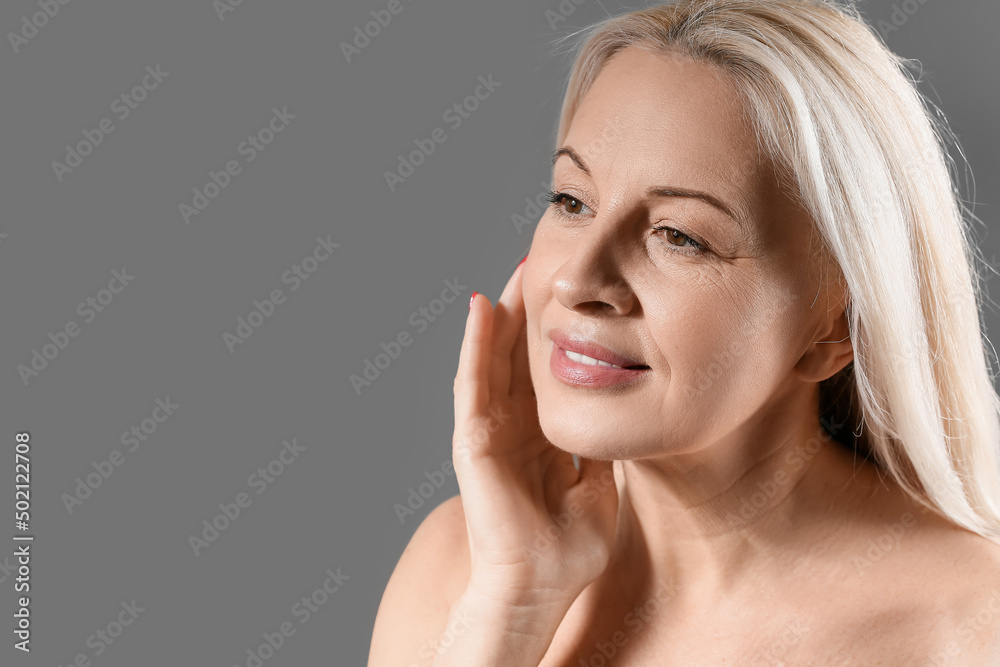 Mature blonde woman with healthy skin on dark background, closeup