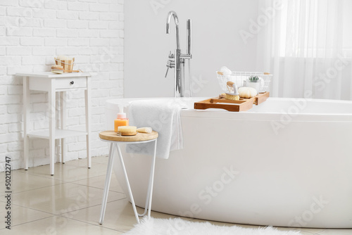 Modern bathtub with tray and different supplies on table in bathroom interior © Pixel-Shot