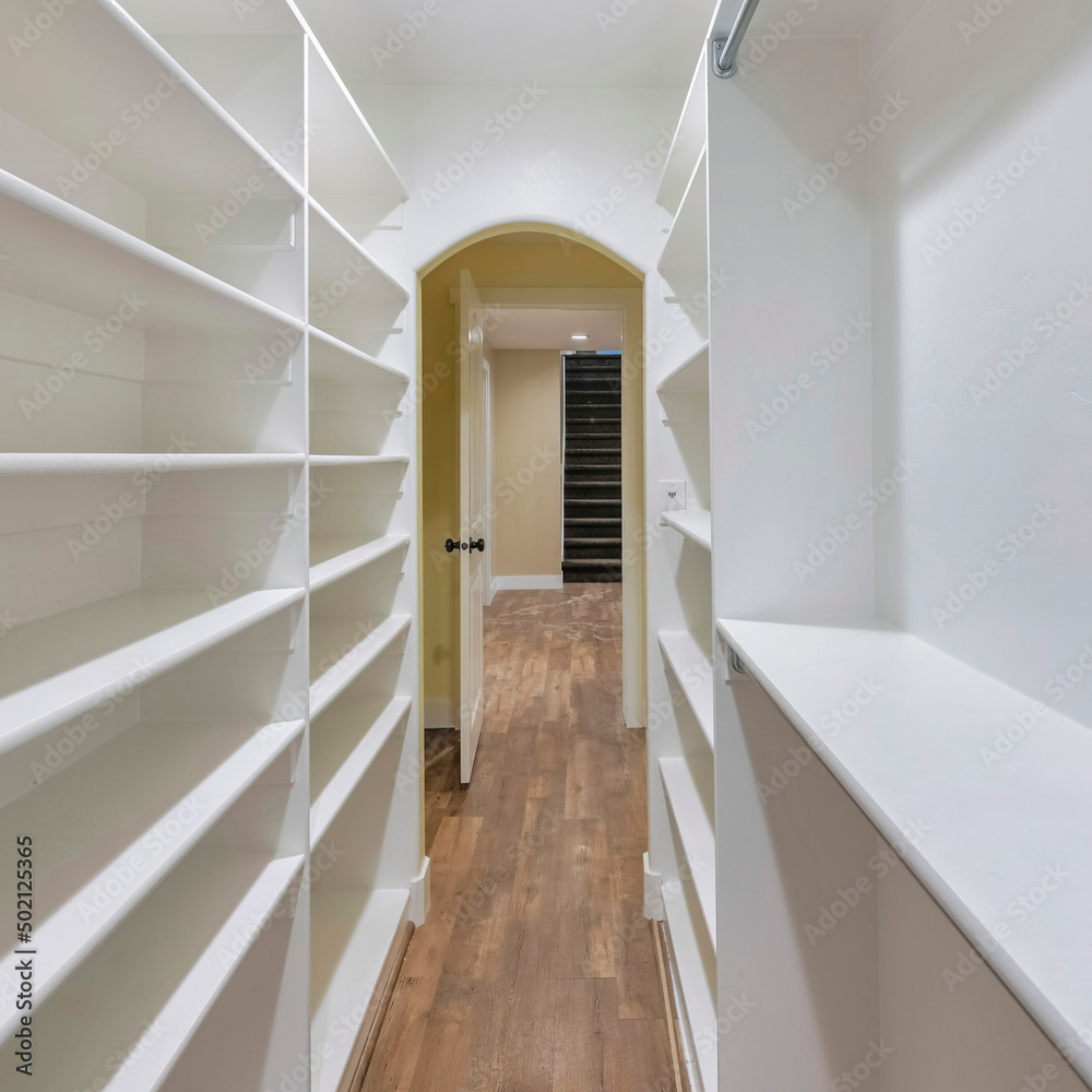 Fototapeta premium Square Narrow walk in closet with wood flooring and shelving units