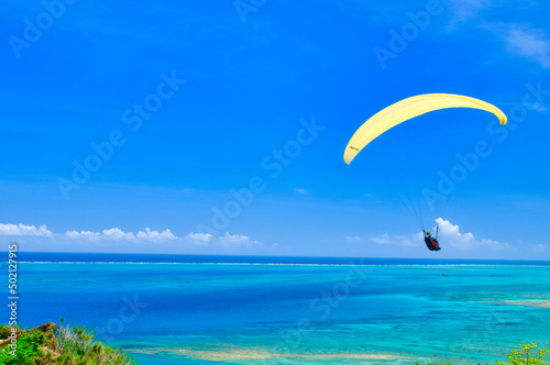 沖縄県知念岬のエメラルドグリーンの海を優雅に飛ぶパラグライダー © Kenji
