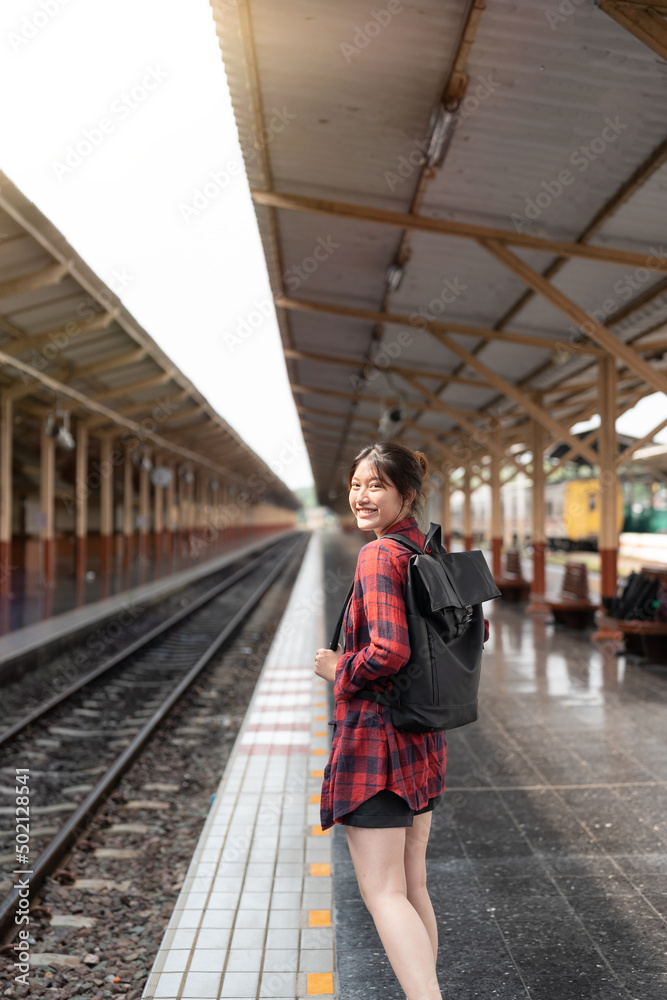 Portrait young Asian woman backpacker traveler walking alone at train station platform with backpack. Asian woman waiting train at train station for travel. Summer holiday traveling concept.