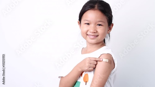 Vaccine concept. Happy Asian little child girl smiling, showing arm with plaster bandage after received, getting COVID-19 vaccine injection. Concept of inoculation, vaccinate, campaign, COVID19, Flu