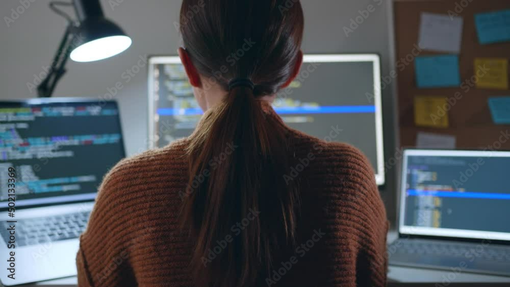 Young Asian woman, developer programmer, software engineer, IT support, wearing glasses working hard at night overtime on computer to check coding in bugging system. Back view