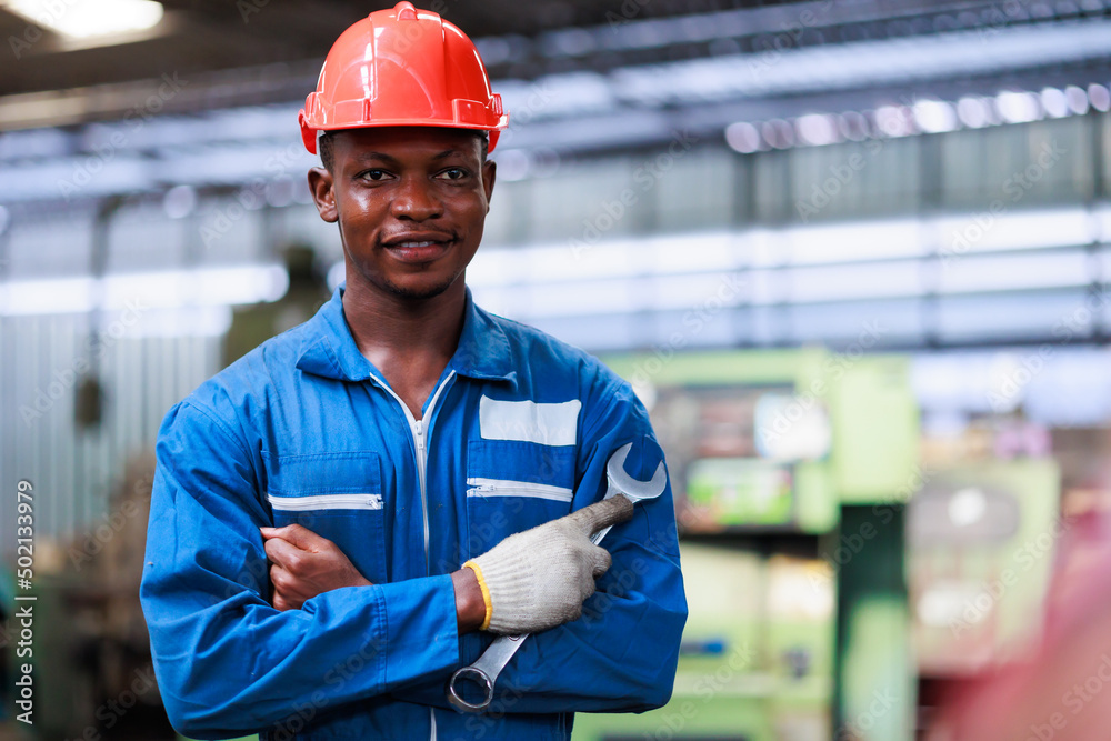 Black man engineer wearing safety hardhat helmet and large wrench working at old factory. Metal lathe industrial manufacturing factory