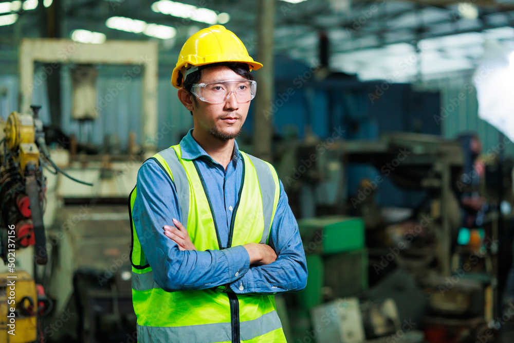 Confident Asian man worker look at camera thumps up. Metal machine in heavy Industry Manufacturing. Asian male factory worker wearing safety hard hat helmet Confident Asian man worker look at camera thumps up. Metal machine in heavy Industry Manufacturing. Asian male factory worker wearing safety hard hat helmet