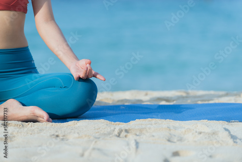 woman practicing yoga alone in the beach. Wearing sport bar. She is barefoot. She is against sea and sand beach.