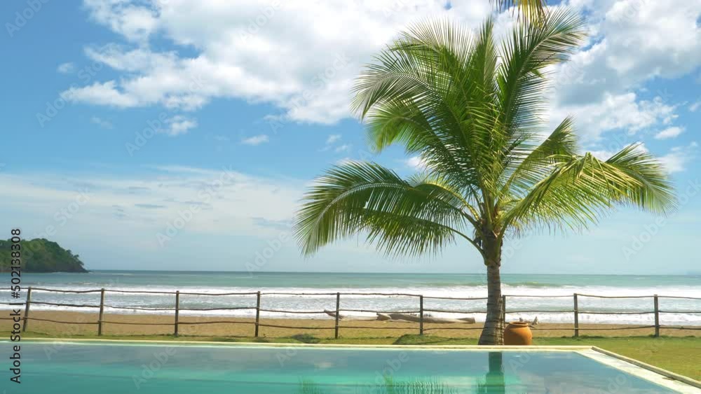 SLOW MOTION: Moving shot of ocean view over swimming pool at exotic resort. Strong swell hitting tropical sandy beach. Exotic summer destination in Panama.