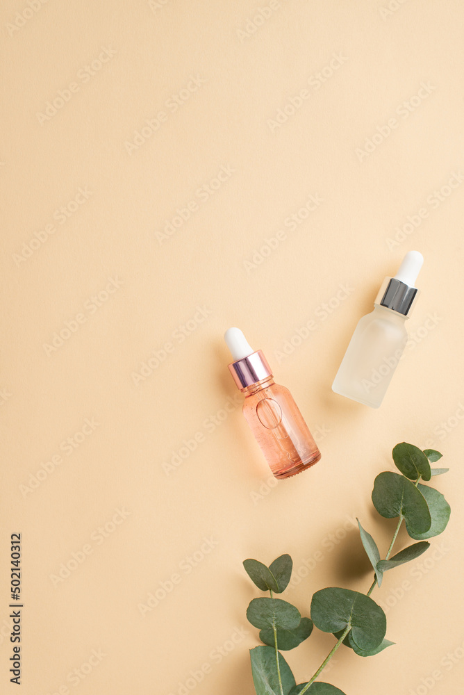 Skincare concept. Top view vertical photo of two transparent pink and white dropper bottles and eucalyptus on isolated pastel beige background with copyspace Skincare concept. Top view vertical photo of two transparent pink and white dropper bottles and eucalyptus on isolated pastel beige background with copyspace