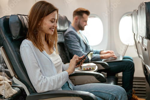 Cheerful woman using mobile phone in airplane photo