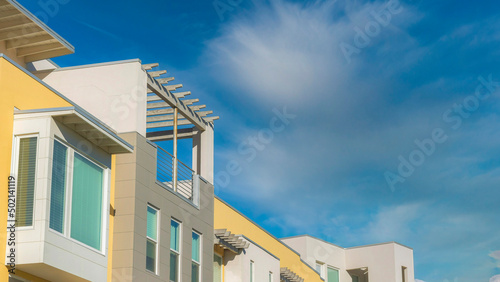 Obraz na plátne Panorama Whispy white clouds Row of apartment buildings with rooftops and pergol