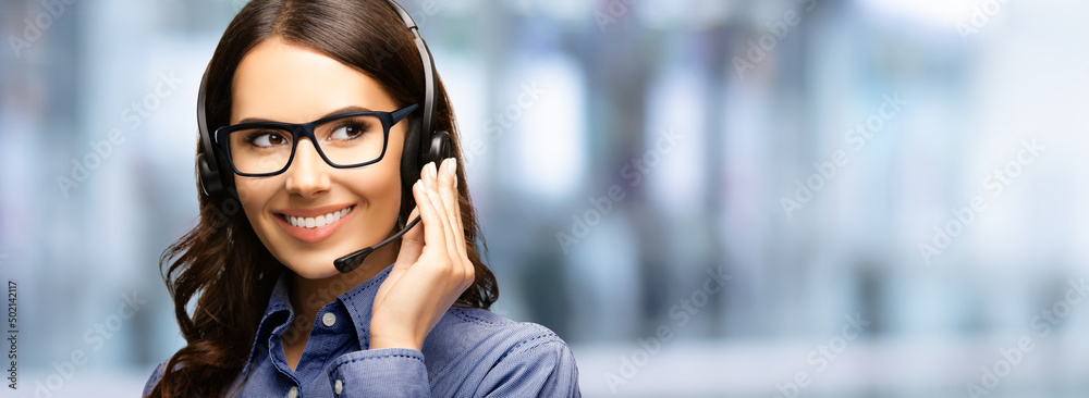 Fototapeta premium Contact Call Center Service. Customer support, sales agent. Caller answering phone operator or businesswoman in headset. Face portrait of brunette woman in eyewear glasses. Blurred office background.
