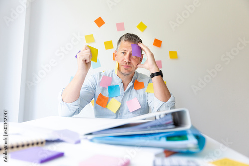 Photography Man sits behind white office desk in front of wall with many colorful notes and