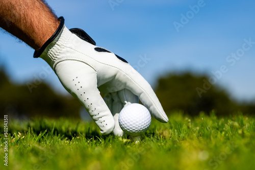 Hand hold golf ball. Golfer man with golf glove. Hand hold golf ball with tee on course, close-up.