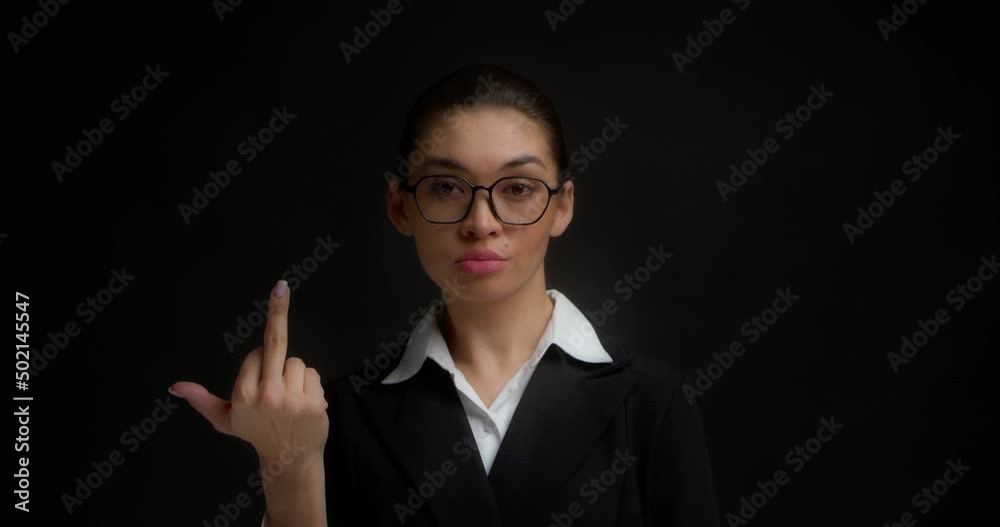 Confident, serious business woman in glasses and office clothes shows the middle finger, fuck you, fuck off, with a haughty face. Isolated on a black background in the studio Confident, serious business woman in glasses and office clothes shows the middle finger, fuck you, fuck off, with a haughty face. Isolated on a black background in the studio