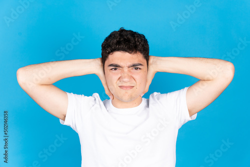 Hispanic teenager boy hands on ears suffering earache isolated on blue background. Stress, anxiety and depression concept. © Egoitz