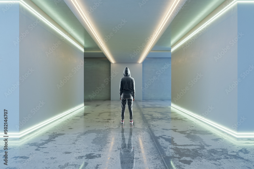Back view of hacker in hoodie in futuristic space corridor interior with white lights. Technology and architecture concept. Back view of hacker in hoodie in futuristic space corridor interior with white lights. Technology and architecture concept.