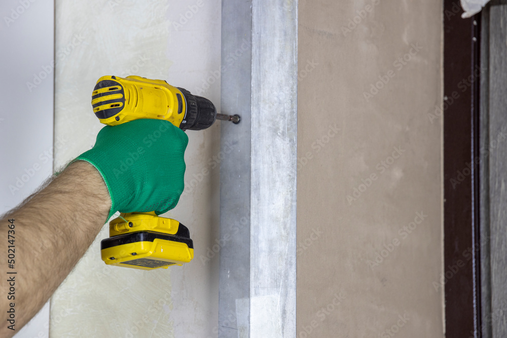 Cordless screwdriver, the worker unscrews the screw from the wall. The man is screwing the rule to the wall. Cordless screwdriver, the worker unscrews the screw from the wall. The man is screwing the rule to the wall.