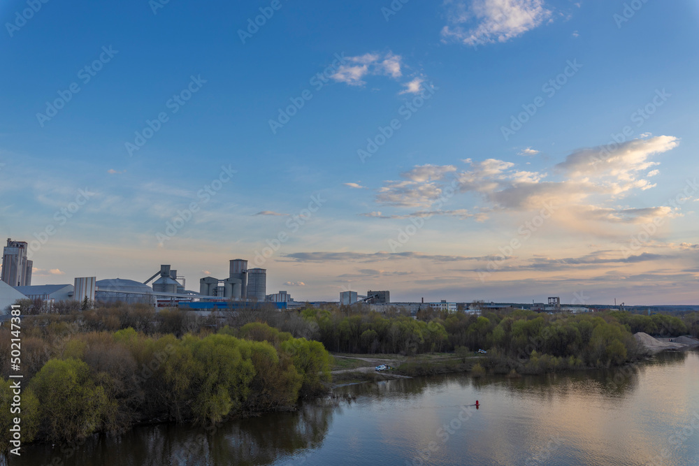 Evening landscape, sunset on the river. View of the industrial zone. Wide river, horizon, clouds are reflected in the water. Sunlight through the clouds. Evening landscape, sunset on the river. View of the industrial zone. Wide river, horizon, clouds are reflected in the water. Sunlight through the clouds.