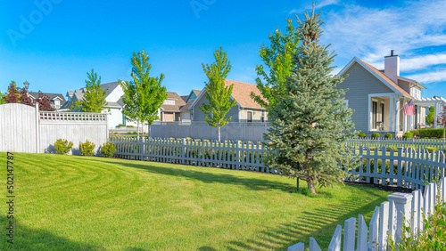 Tableau sur toile Panorama Whispy white clouds White picket fence of a yard with green lawn and pi