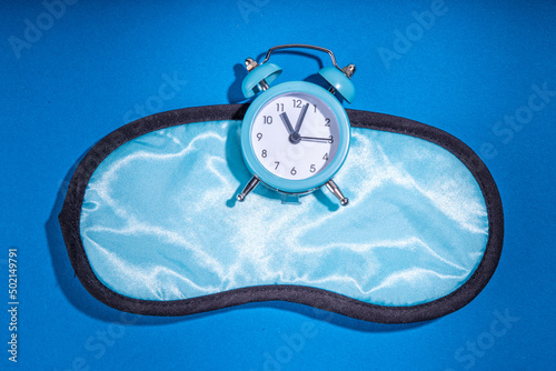 Healthy deep sleep background. Circadian rhythms, circadian clocks and biological clock concept. Blue fabric sleep mask with an alarm clock on dark blue background. Simple flatlay copy space photo