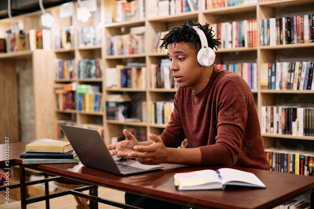 Black male student making video call via laptop while learning in library, Black male student making video call via laptop while learning in library,