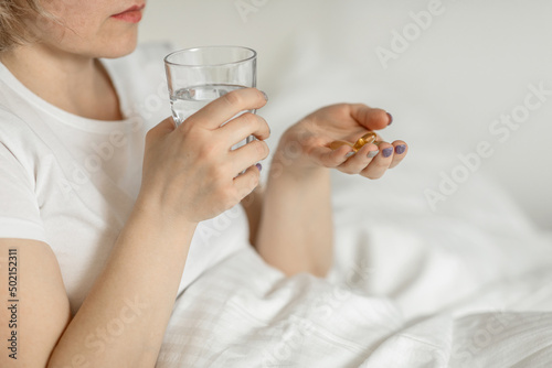 A white faceless woman, a middle-aged woman holds a glass of clean water and vitamins in her hands, sitting on the bed. the concept of health and beauty care