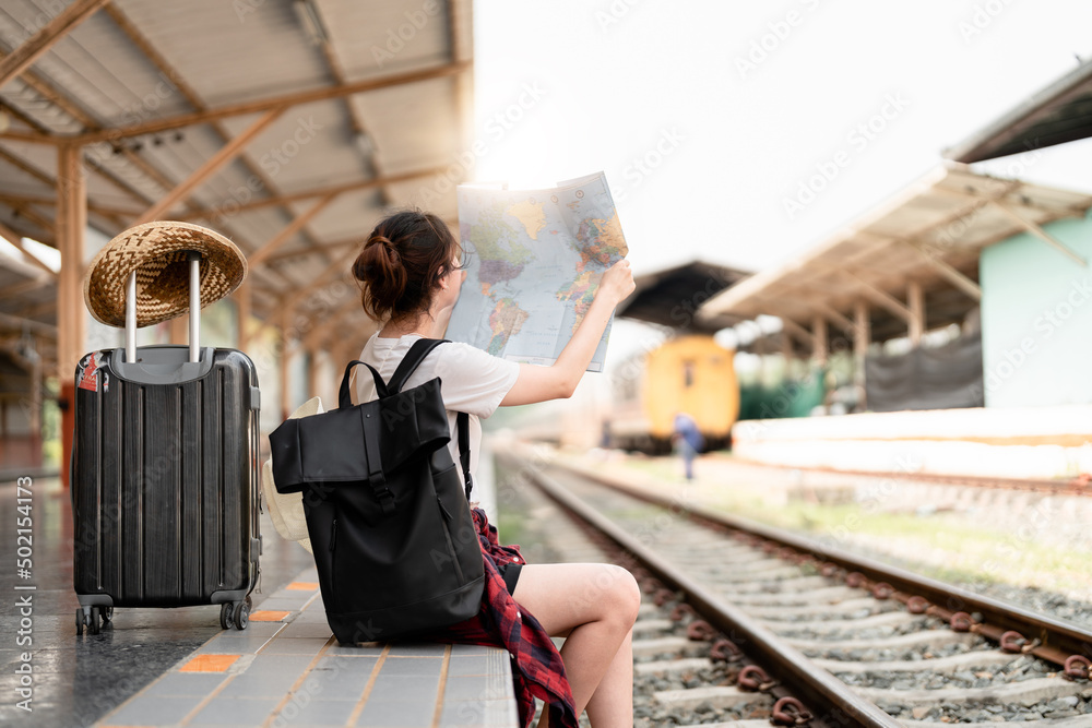 Young woman traveler with backpack looking to map while waiting for train, Asian backpacker on railway platform at train station. Holiday, journey, trip and summer summer travel concept