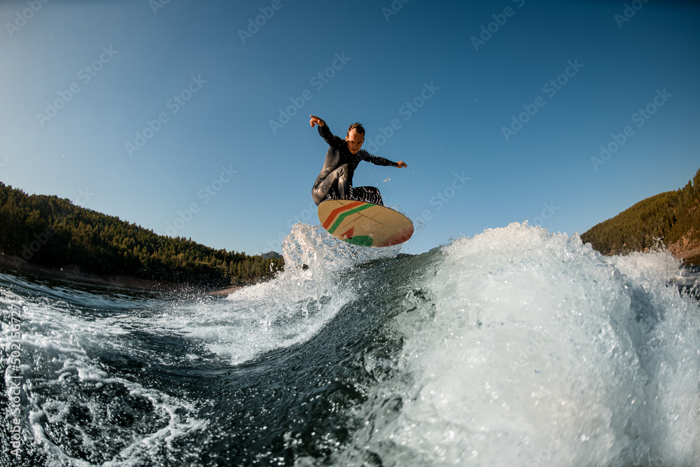 Active man with the wakesurf skillfully jumping over splashing wave