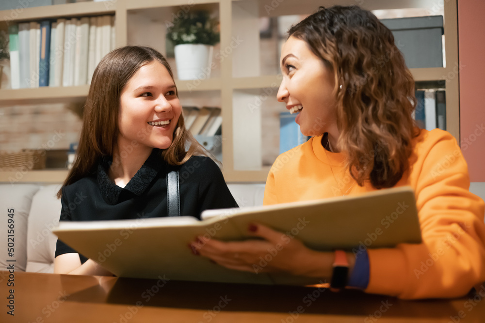 Two girl friends chat and choose food and drinks on the menu while sitting in a restaurant Two girl friends chat and choose food and drinks on the menu while sitting in a restaurant