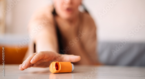 A girl suffering from an asthma attack due to allergies reaches for an inhaler while sitting on the sofa in the living room of the house. the concept of allergy control photo