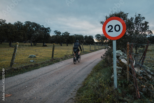 Cyclist riding by speed limit sign on road at sunrise photo