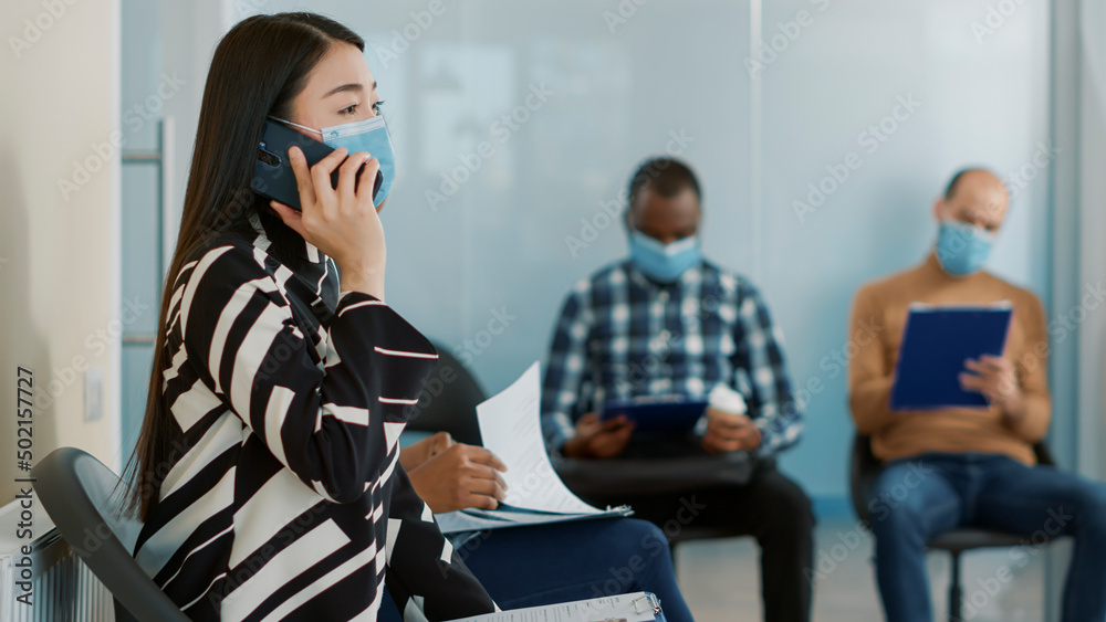 Asian woman talking on phone call and waiting to join job interview with HR team, sitting in office lobby and using smartphone. Female candidate talking on mobile phone at employment meeting.